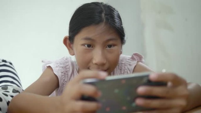 快乐的亚洲女孩玩网络游戏与她的兄弟在家里，生活方式的概念智能手机。