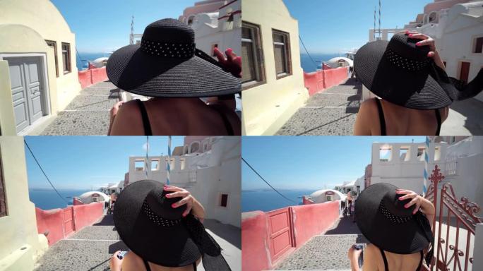 在希腊圣托里尼岛Oia的旅游度假中，戴帽子的优雅旅游女人。快乐的年轻女子走在狭窄的街道上，参观希腊岛