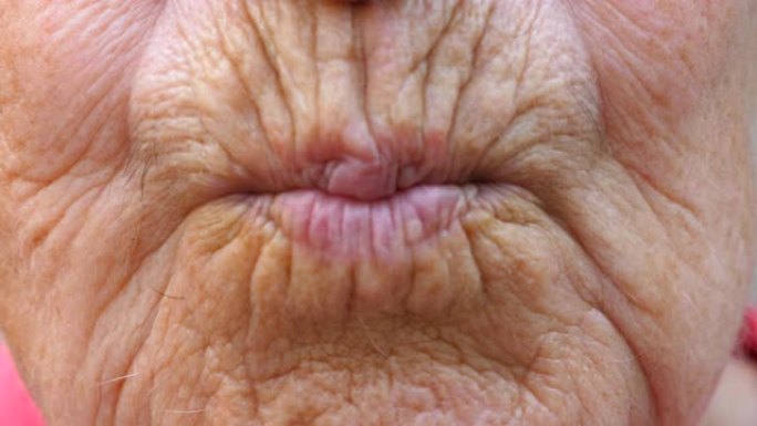 关闭成熟祖母的嘴唇。奶奶的嘴把空气吻送进镜头。皮肤皱纹的高级女性做接吻手势。慢动作