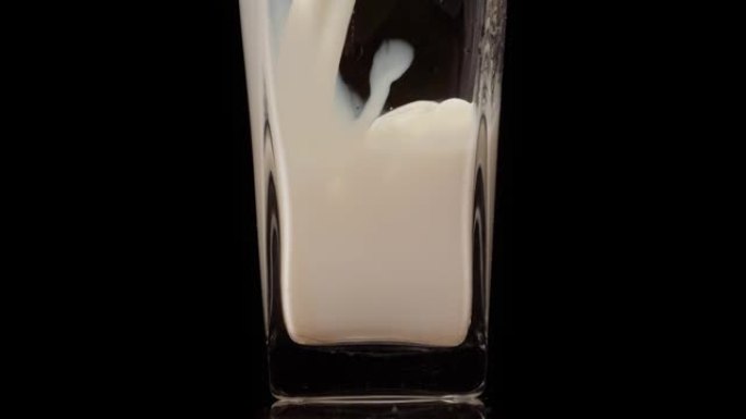 味道很好。将新鲜牛奶倒入黑色背景下的透明玻璃中的超级慢动作镜头。特写。乳制品概念