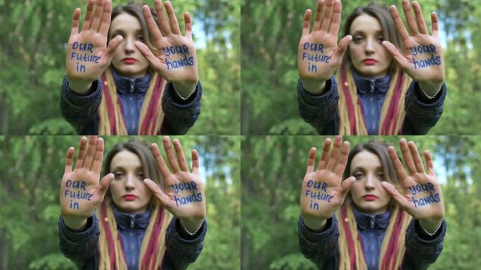 梳着长发的现代严肃女孩在绿树背景上举起手，上面写着“我们的未来在你手中”的口号。责任，气候变化概念