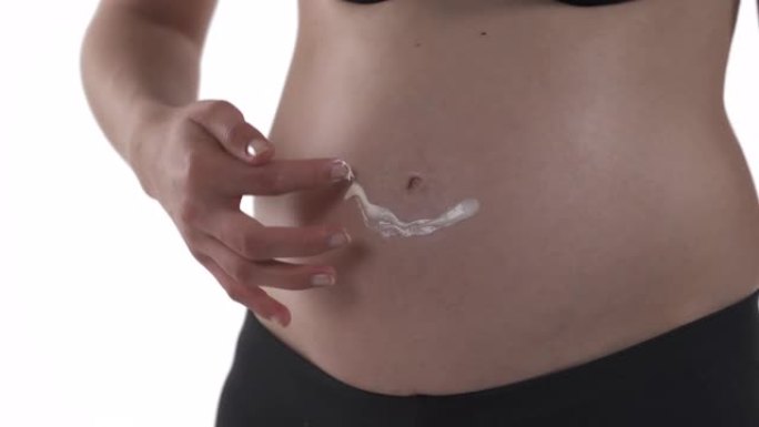 特写的怀孕白人妇女的肚子。准妈妈用润肤霜在肚子上画微笑标志。孕期护肤概念。孤立在白色背景上。