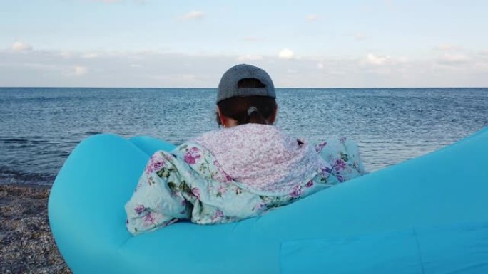 海滩上的一个女孩坐在充气吊床上。