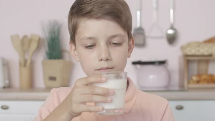 调皮的小男孩在玻璃中闻到牛奶的特写镜头，表情不满意。可爱的高加索孩子早上拒绝喝乳制品的肖像。不听话的