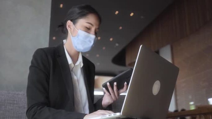 年轻的亚洲女性企业住在咖啡馆，她戴着口罩保护病毒空气污染的安全旅行和工作与她的笔记本电脑突然她停止与