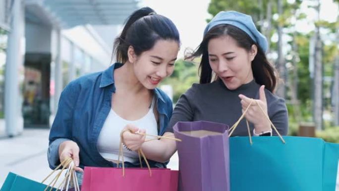 微笑的年轻亚洲女人，购物中心背景上的彩色包。使用智能手机在线购物，站在商场大楼时微笑。生活方式概念。