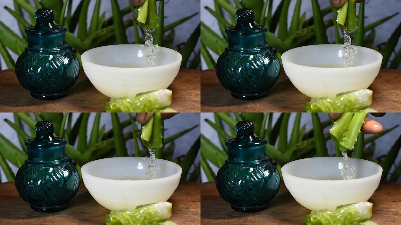 将小的仿古蓝色玻璃锅放在木制桌子上，将凝胶从芦荟叶中提取，并在芦荟植物的背景上的白色碗中提取凝胶。