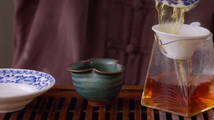 师傅往盖湾倒热水，在木托盘上冲泡绿茶。仪式上，热茶通过筛子倒入公平投手。中国茶从玻璃锅倒到碗喝。