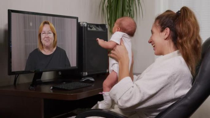 母亲和婴儿在享受家庭联系的新生婴儿面前挥舞着电脑进行视频聊天。