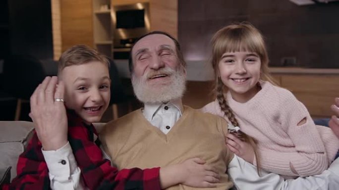 迷人的受人尊敬的退休胡须男子的前视图，与他的两个微笑着快乐的漂亮孙子在房间背景上摆姿势