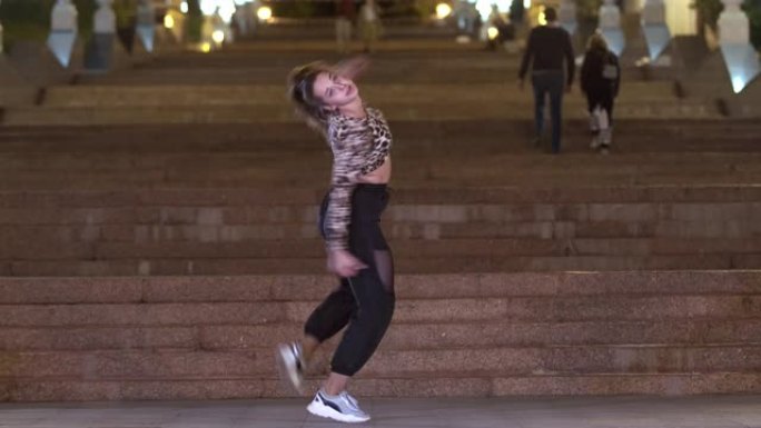 穿着豹纹t恤的漂亮女孩晚上在一个古老的巨大石楼梯前在户外跳街舞