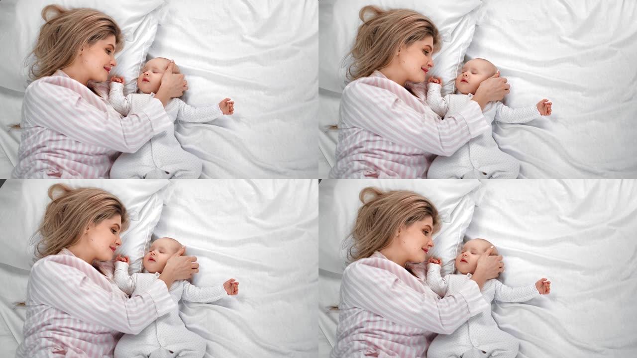 顶视图愉快的母亲抚摸着躺在白色床上睡觉的可爱的小宝宝。4k龙红相机