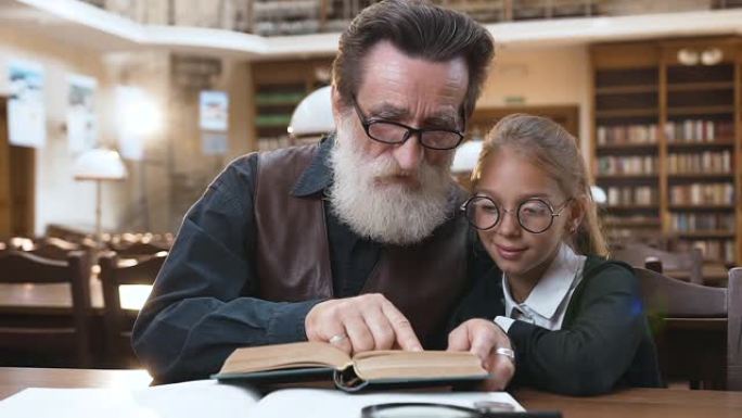 善良的白胡子的老爷爷坐在图书馆里，和他可爱的十几岁的孙女一起看书