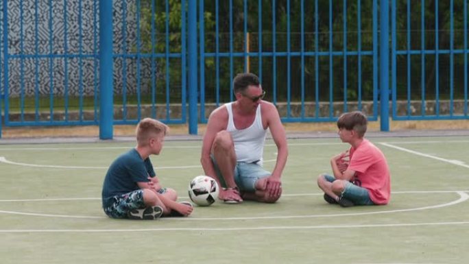足球教练在夏季城市营地的操场上积极与男孩交谈。