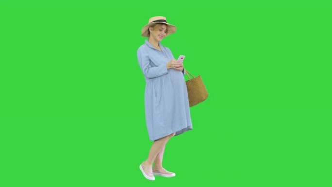 第9个月的孕妇在绿屏上使用智能手机，色键