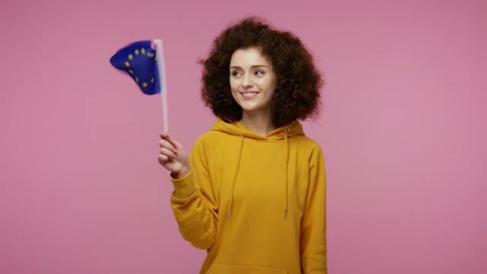 快乐的女学生发型在帽衫挥舞着欧盟旗帜，微笑着，欢呼民主的法律