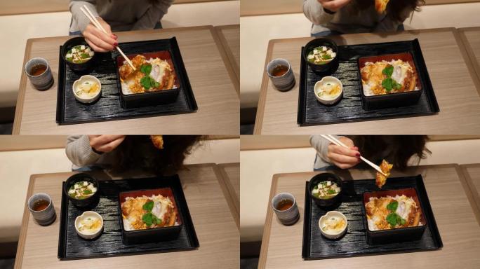 女人开始吃日本餐，用筷子拿一块猪排