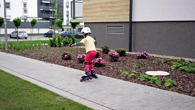 一个小女孩在公寓楼的院子里溜冰。这个孩子刚刚开始掌握溜冰鞋，所以他经常摔倒