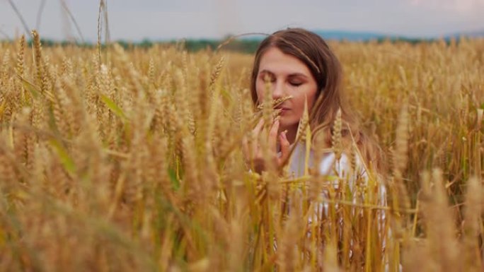 一个年轻的女孩走过田野的麦穗。美丽的无忧无虑的女人享受大自然，在麦田里用手触摸