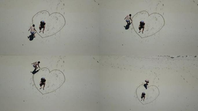 在印度尼西亚毛米尔附近的一个小岛上，一对夫妇在白色沙滩上画了一颗心的无人机镜头。快乐和粗心的时刻。波