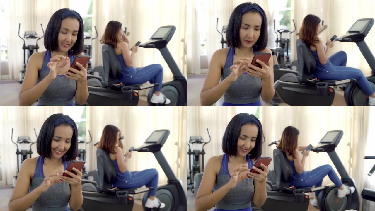 两名年轻的亚洲女性使用手机在健身馆的社交媒体上自拍和发短信。