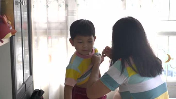 一位亚洲母亲正在帮助她的儿子打扮。早晨，自然光