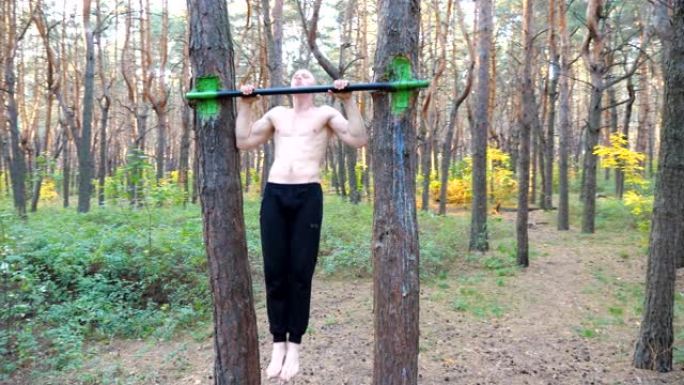 强壮肌肉的男人在美丽的森林里做引体向上。男性运动员在大自然的单杠上锻炼。运动男户外训练。运动的概念和