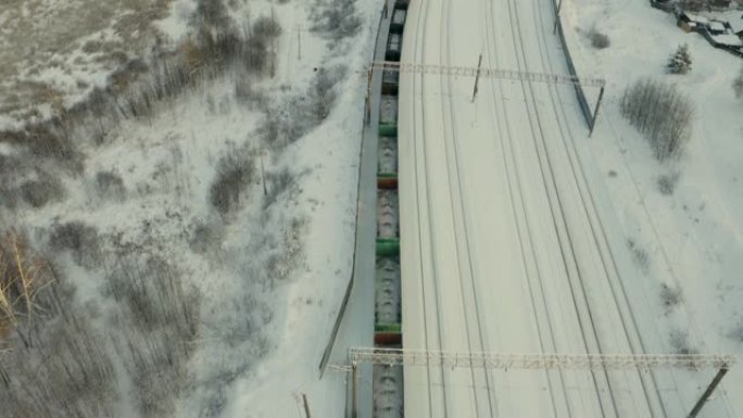 货运列车上的无人驾驶飞机的俯视图，一列长长的火车，日落时接近车站，冬天在树林中。雪地里的树。