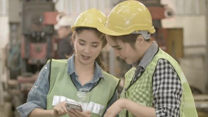两名在重工业制造工厂工作的工程工人一边看手机一边交谈。在装配和生产线上聊天，一起计划项目。