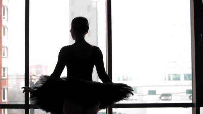 城市建筑背景下的芭蕾。剪影芭蕾舞演员做出优美的动作。美丽的古典舞。穿着黑色短裙和尖头鞋。慢动作。斯蒂