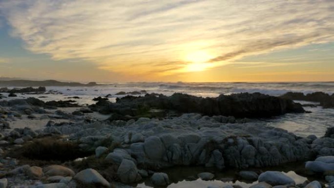 慢动作太平洋海浪在暴风雨天气下在加利福尼亚州蒙特利半岛的太平洋格罗夫的日落天空下滚滚并在多岩石的海岸