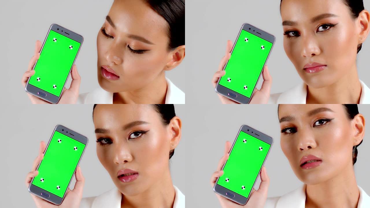 美丽的亚洲女商人展示绿屏智能手机，看着相机