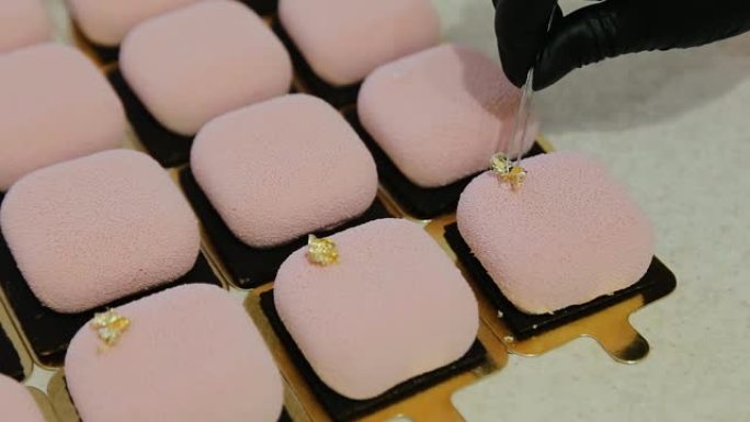 糖果店在现代慕斯蛋糕的顶部添加了可食用的金色箔装饰元素，并带有粉红色的丝绒糖霜。优雅的方形丝绒慕斯蛋