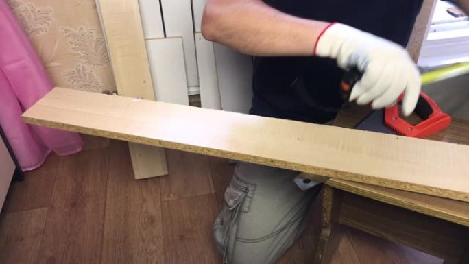 一个人用卷尺测量木板。在家做家具。
