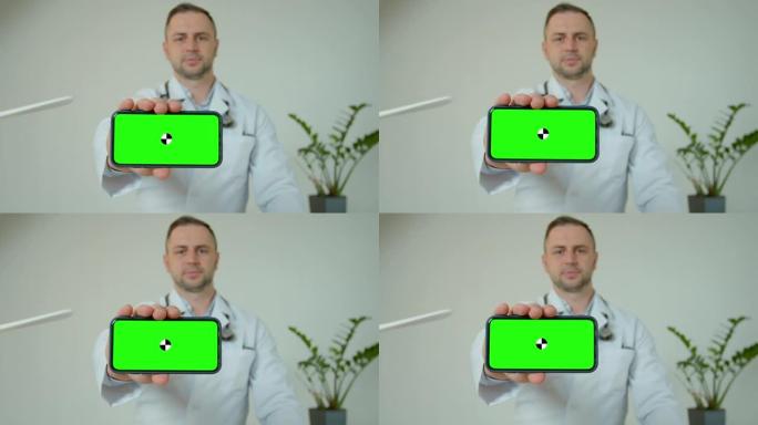 男性医疗专业人员展示带绿屏的移动智能手机。医生拿着绿屏手机对着镜头。科学家持有的电话绿屏。男医生演示