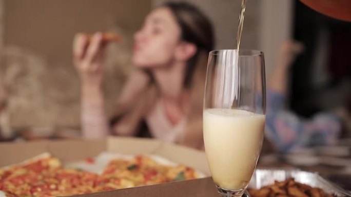 泡沫啤酒倒入透明玻璃杯中，在背景中，一个女孩吃披萨
