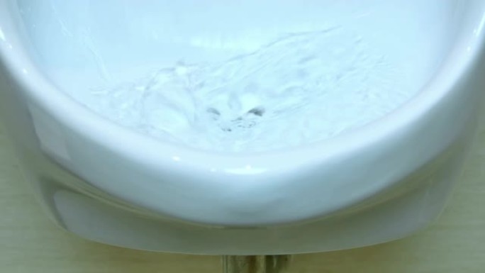 从陶瓷小便池流向马桶孔的水的特写视图。
