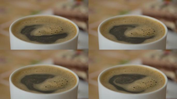 人手搅拌杯热巧克力。新鲜的早晨咖啡特写。慢动作。牛奶热巧克力在白杯。男人在一杯芳香的咖啡特写中搅拌糖