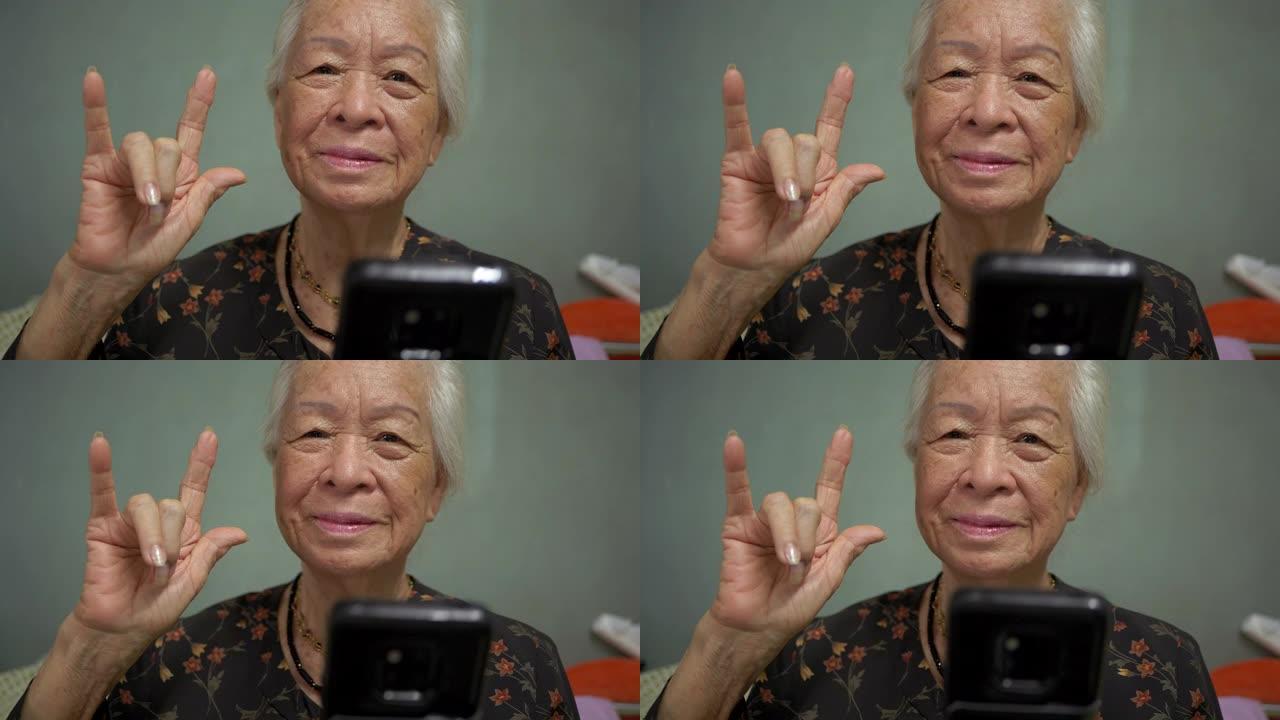 多莉万向节镜头: 快乐的亚洲高级女性在卧室里用手机示意再见，竖起大拇指，爱。聊天和观看视频。概念: 