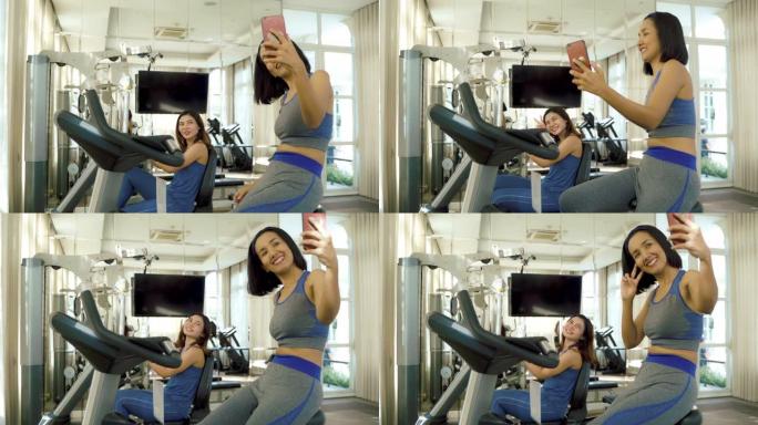 两名年轻的亚洲女性使用手机在健身馆的社交媒体上自拍和发短信。