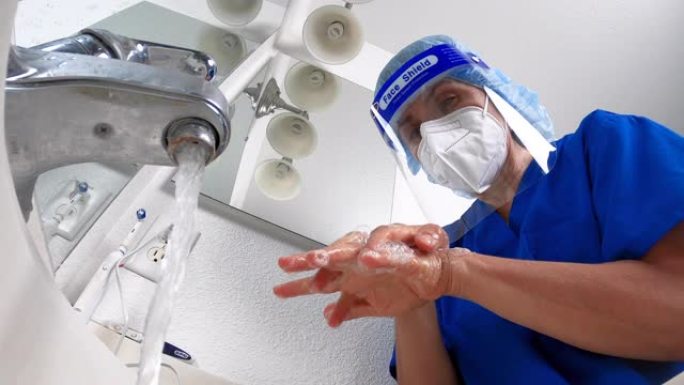 戴着防护口罩和面罩的女医护人员洗手