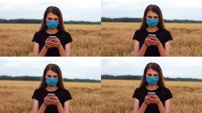 美丽的年轻女子戴着防毒面具，站在田野里看手机。
