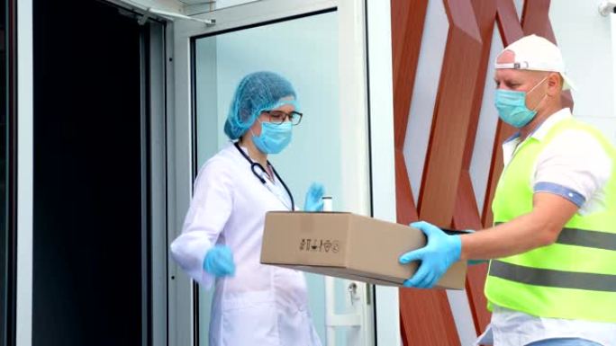 冠状病毒爆发期间，将带有医疗设备的包裹运送到医院。快递员戴着防护口罩，手套，正在将纸板箱交给医生，医