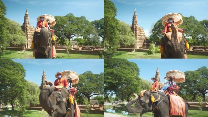 游客，年轻的亚洲妇女和朋友前往大城府的古老历史建筑。泰国曼谷附近。游客乘坐大象穿越城市