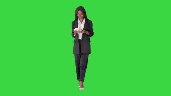 快乐的非洲裔美国妇女在绿色屏幕上行走时数钱，色度键