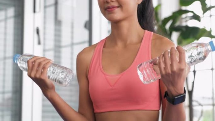 亚洲女性在家使用水瓶作为哑铃重量训练在线课程，带平板电脑。特写镜头