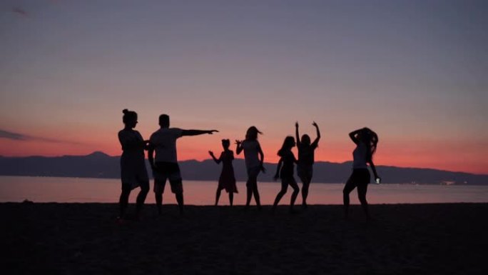 美丽的海上日落背景，一群快乐快乐的朋友在海边赤脚跳舞。跳舞的人举起双手的轮廓。海滩派对背景