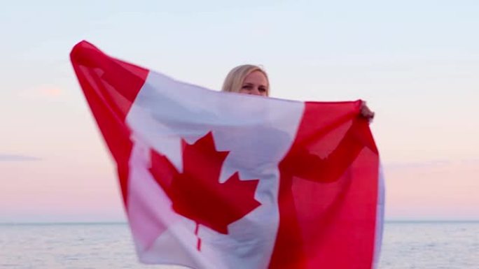 4 k。微笑的女人挥舞着加拿大国旗在户外海洋海洋日落在夏天-加拿大国旗，国家，爱国主义，7月1日