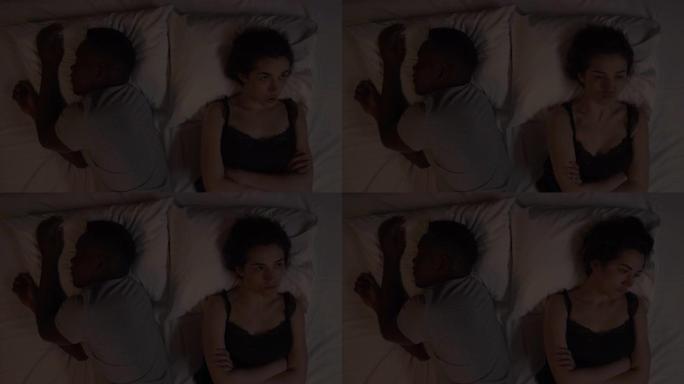 多种族夫妇晚上躺在床上的特写镜头。高加索女孩的景象和摇头，因为她的非洲男友正在睡觉