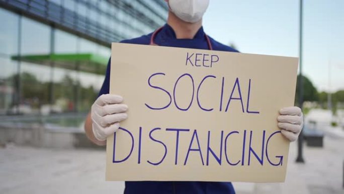负责任的男护士在新型冠状病毒肺炎大流行期间举着标语 “保持社交距离”